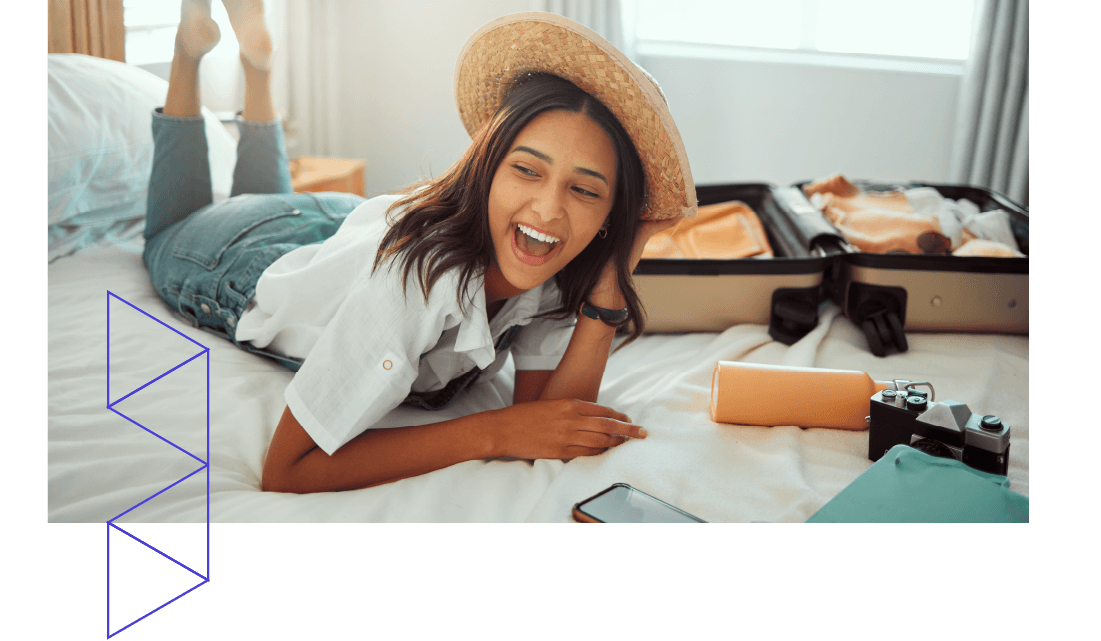 A smiling young woman in a straw hat lying on a hotel bed next to an open suitcase. A smiling young woman in a straw hat lying on a hotel bed next to an open suitcase.