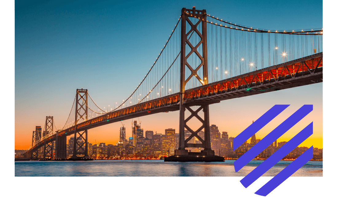 Large bridge at sunset with a city skyline behind it. 