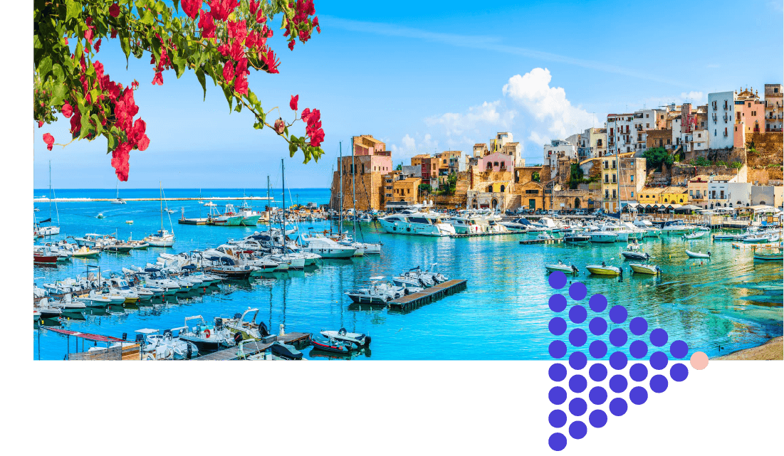 A sunny harbor full of boats, with colorful, rustic buildings along the shore.