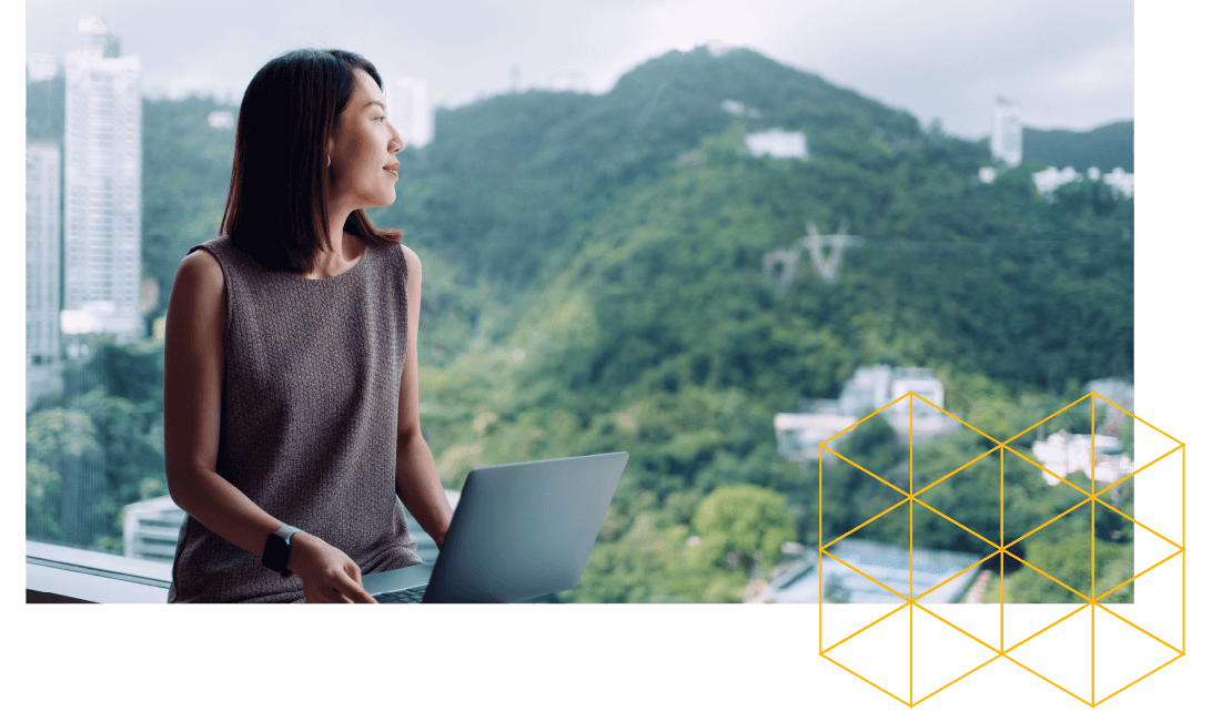 Professional woman with a laptop looking out of a window with green hills outside.