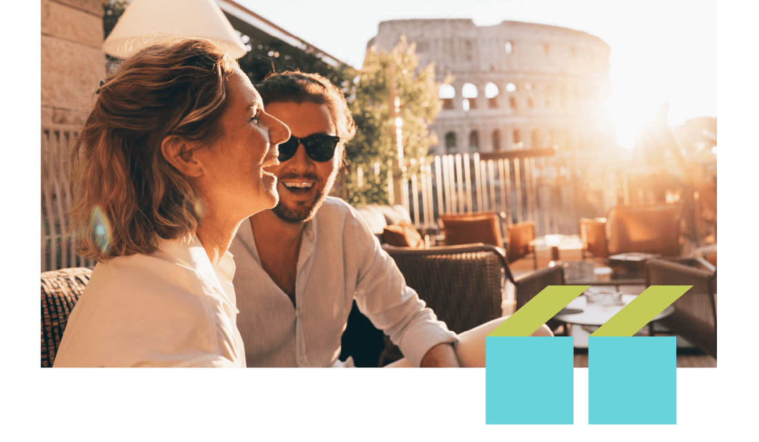 A smiling couple in an outdoor restaurant in Rome with the Colosseum in the background.