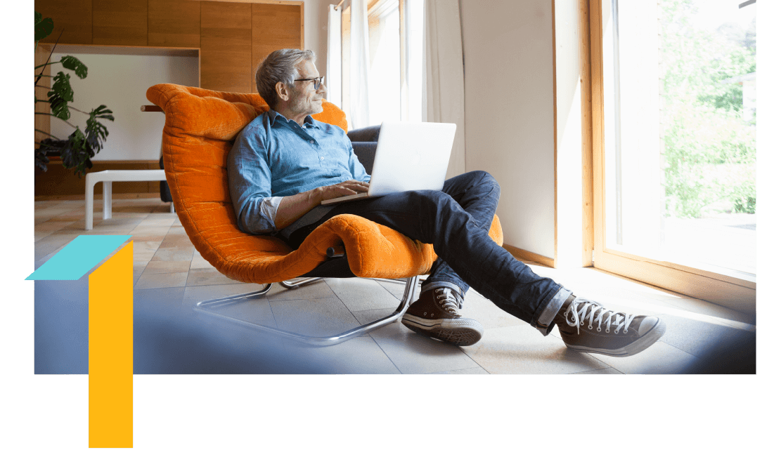 Man in an orange chair with a laptop in his lap, looking out of a window. 