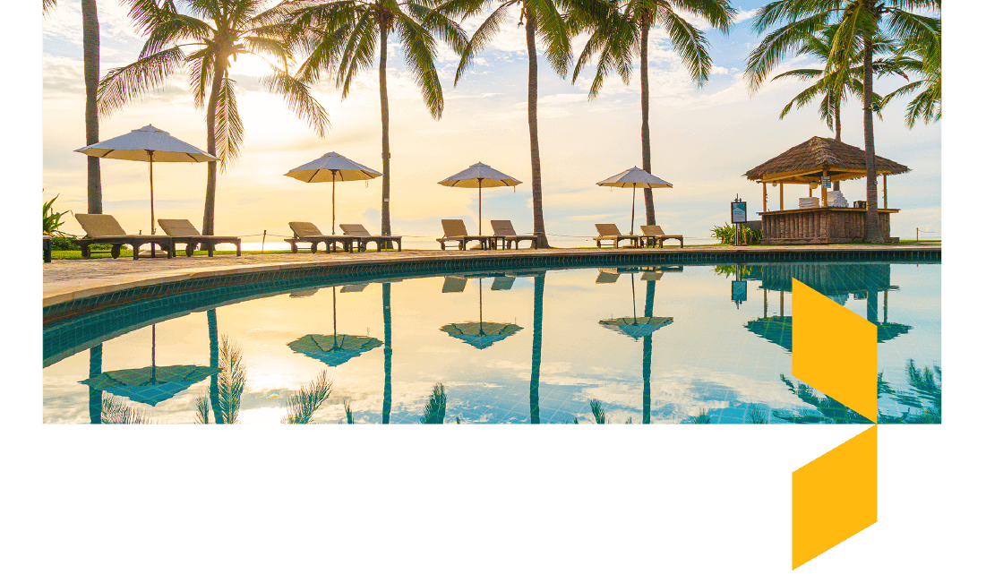 Swimming pool at sunset with sun loungers and palm trees around the edge. 