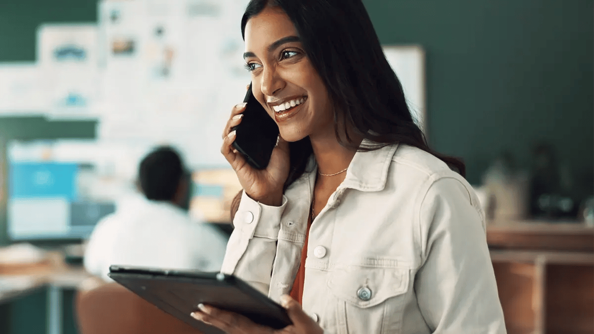 A smiling person talking on the phone with a customer, and holding an IPad to take notes.