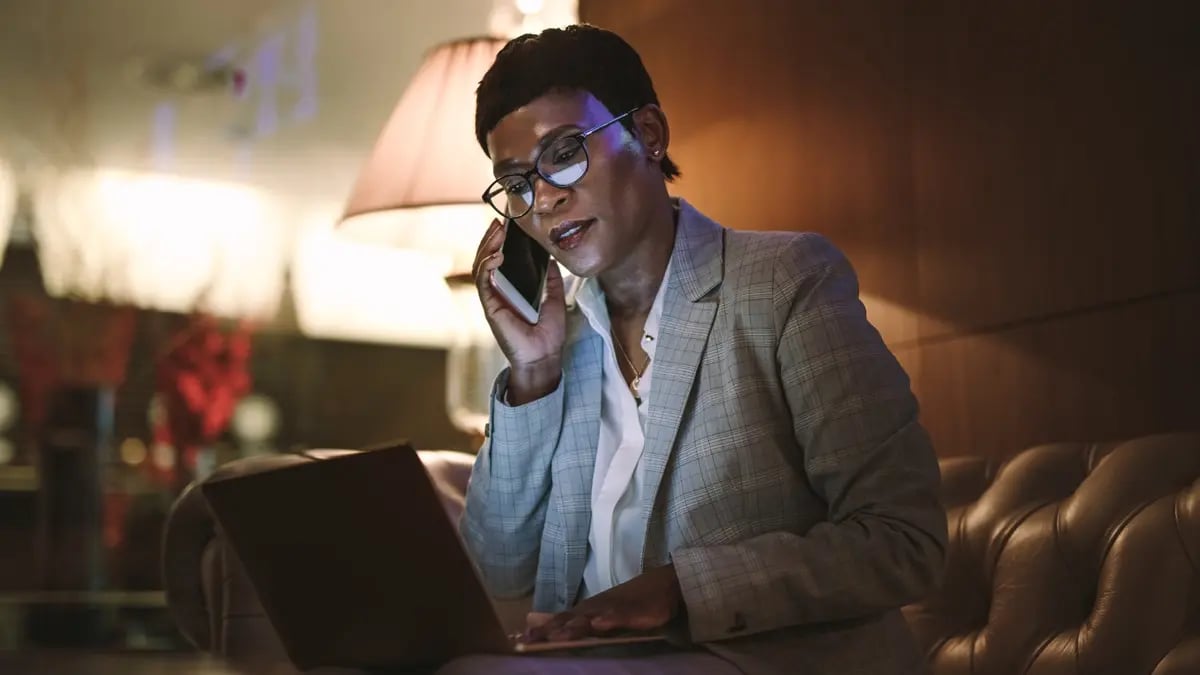 A dark skin woman talking over the phone in a darker hotel lobby.