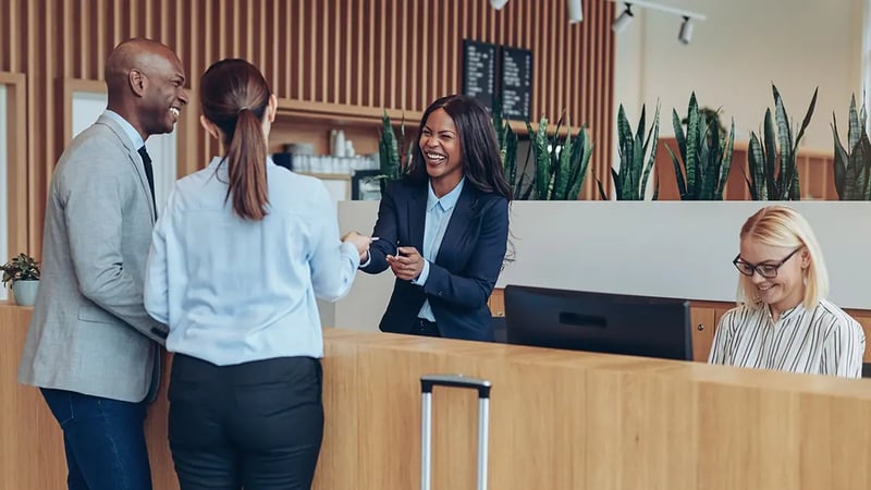 Two people checking in at a hotel speaking to a concierge and smiling.