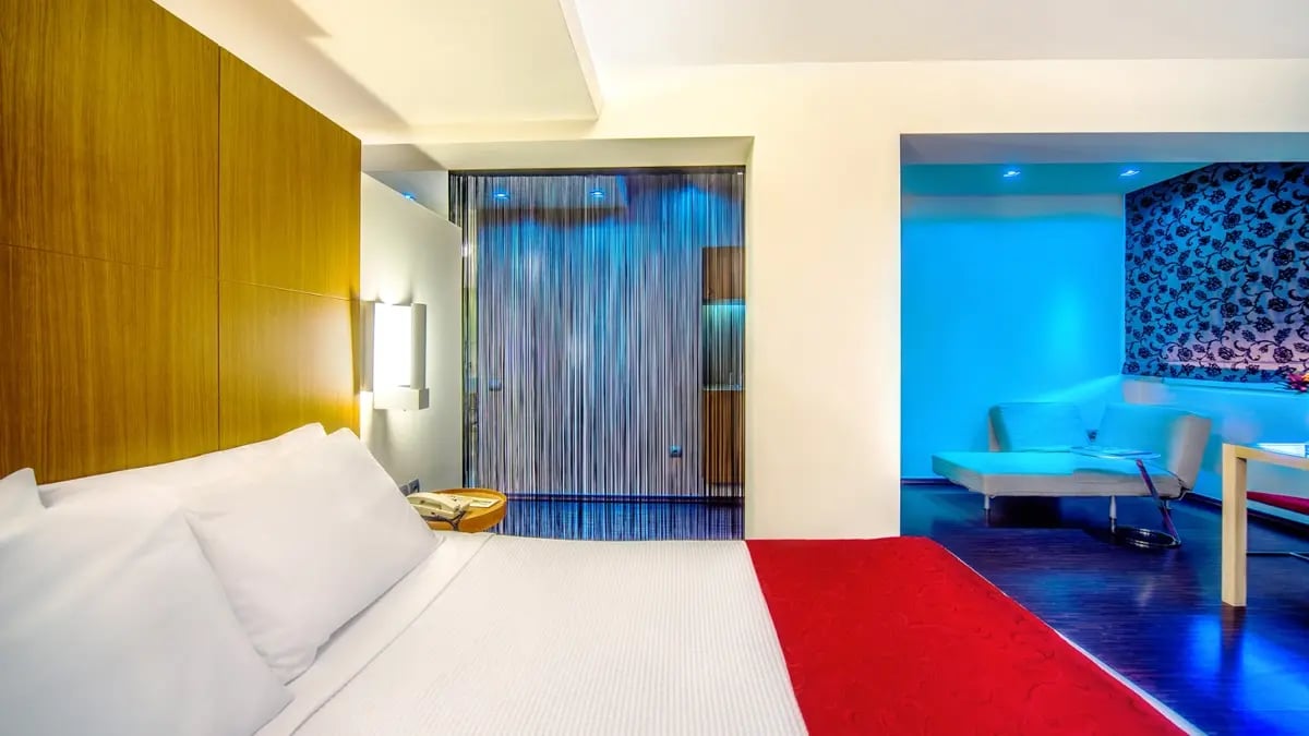 A modern-looking hotel room with a double-bed and light blue lightning in the background.