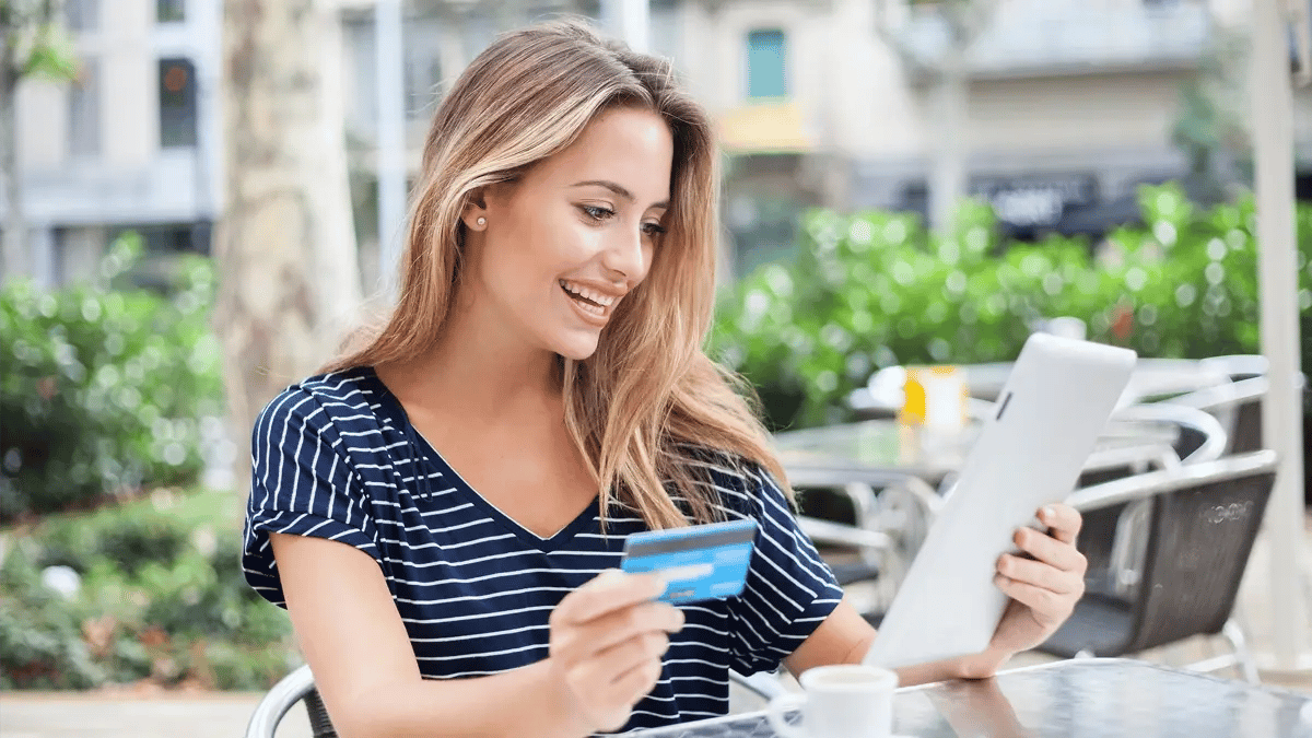 A person sitting at an outdoors coffee shop, looking at the menu and holding their credit card.