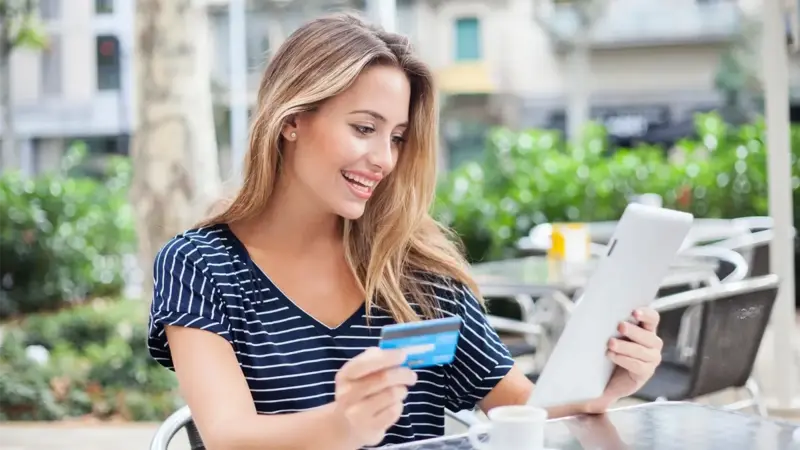 A person sitting at an outdoors coffee shop, looking at the menu and holding their credit card.