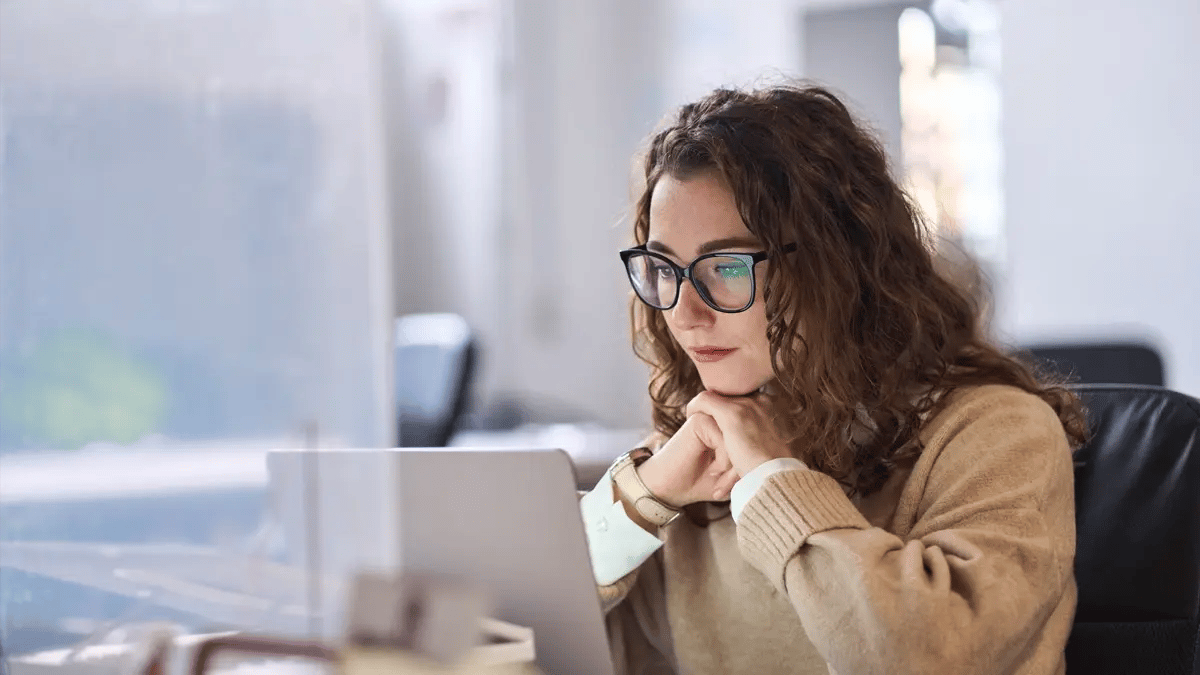 A lady with glasses sitting in an office looking at her computer.