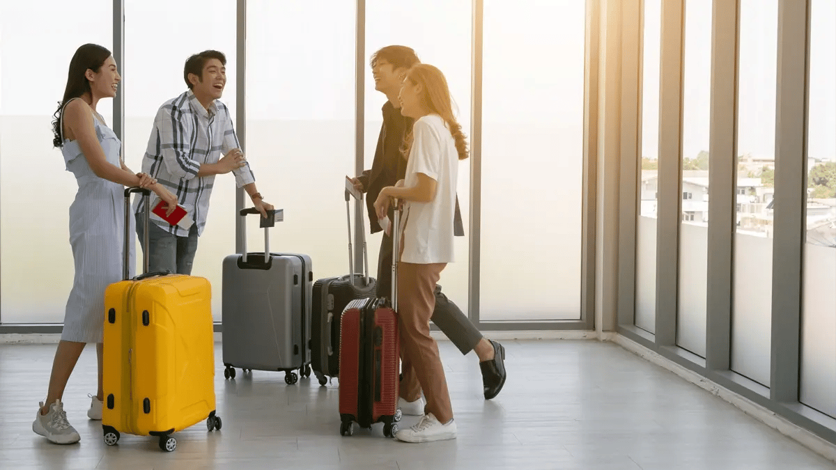 A group of friends with their suitcases laughing at a grey room at the airport.