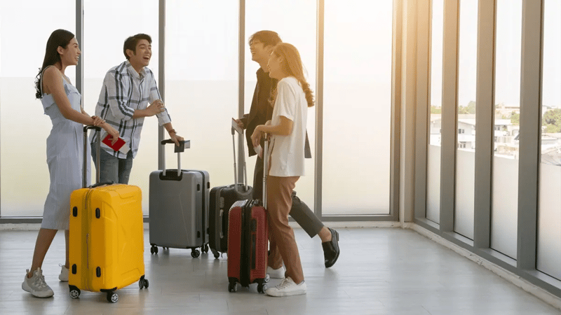 A group of friends with their suitcases laughing at a grey room at the airport.