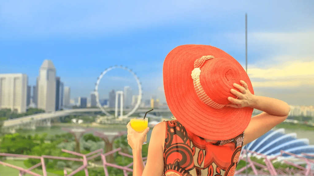 A lady with a big red hat and colorful clothes with an orange juice at hand looking towards Las Vegas' city line.