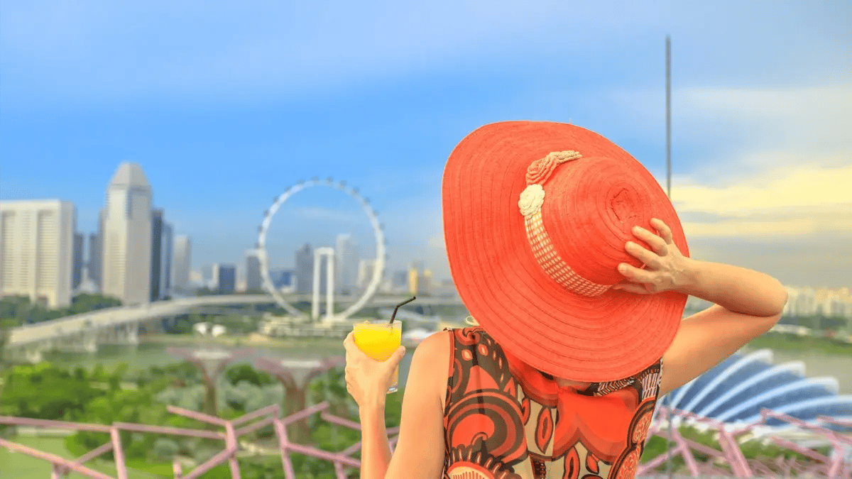 A lady with a big red hat and colorful clothes with an orange juice at hand looking towards Las Vegas' city line.