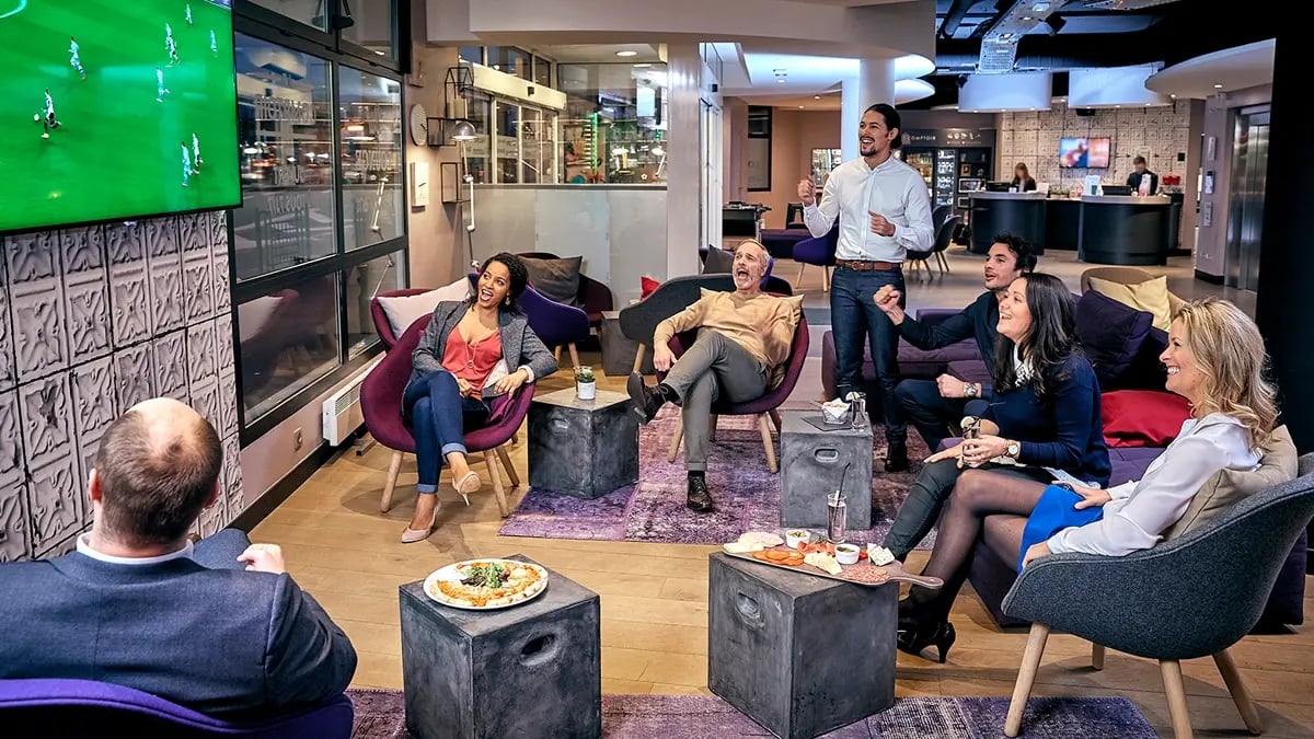 A group of people enthusiastically watching a soccer's game at a modern hotel's lobby.