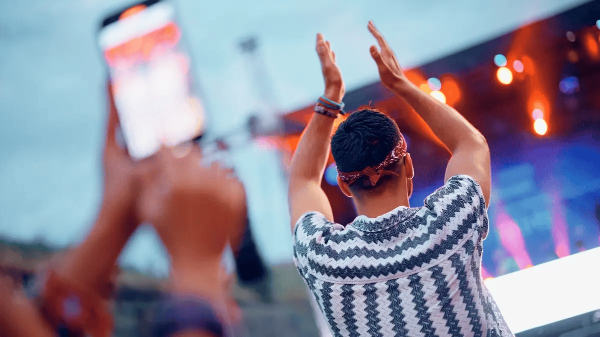 A man clapping with his hands up at a concert. Photo is taken from behind.