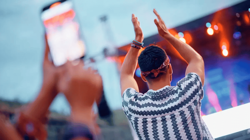 A man clapping with his hands up at a concert. Photo is taken from behind.