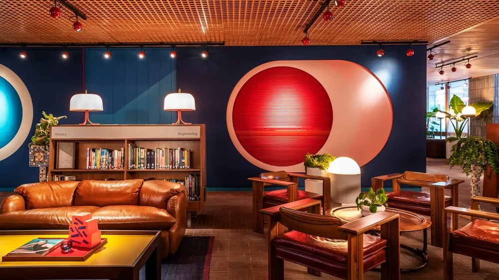 A colorful and artistically looking hotel lobby with leather brown sofas, comfortable chairs, and books in the background.