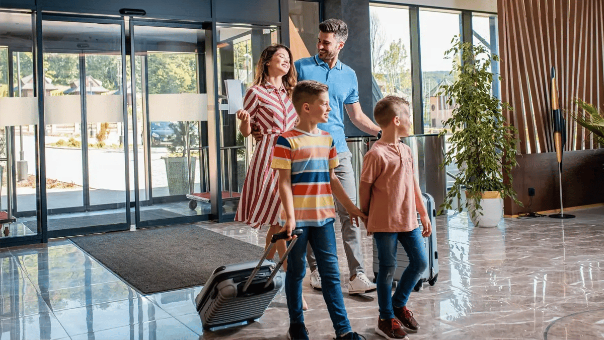 A family of 4 walking in a hotel lobby with their suitcases.