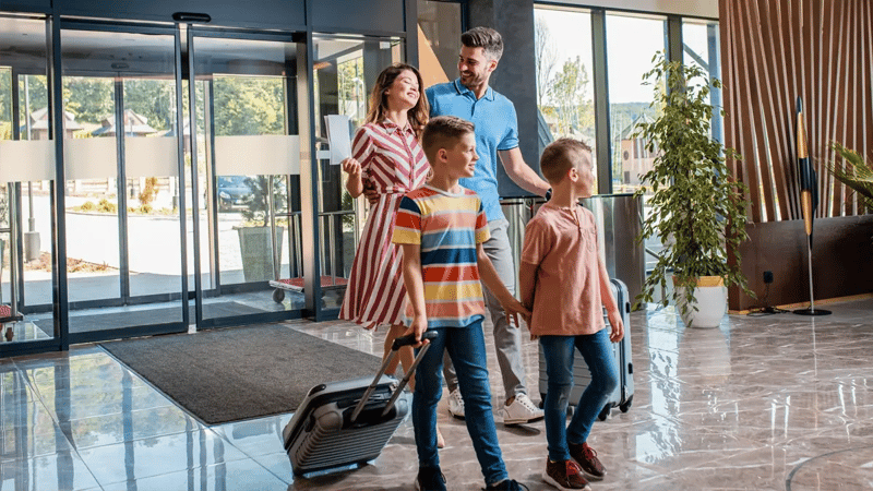 A family of 4 walking in a hotel lobby with their suitcases.