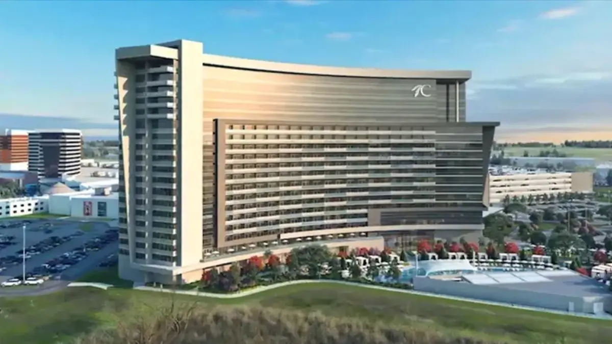 A large greyish hotel in a wave-like shape with a green area and a swimming pool at the front, and parking lots in the back.