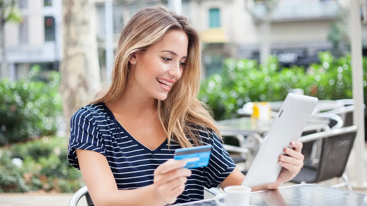 A person sitting at an outdoors coffee shop, looking at the menu and holding their credit card.