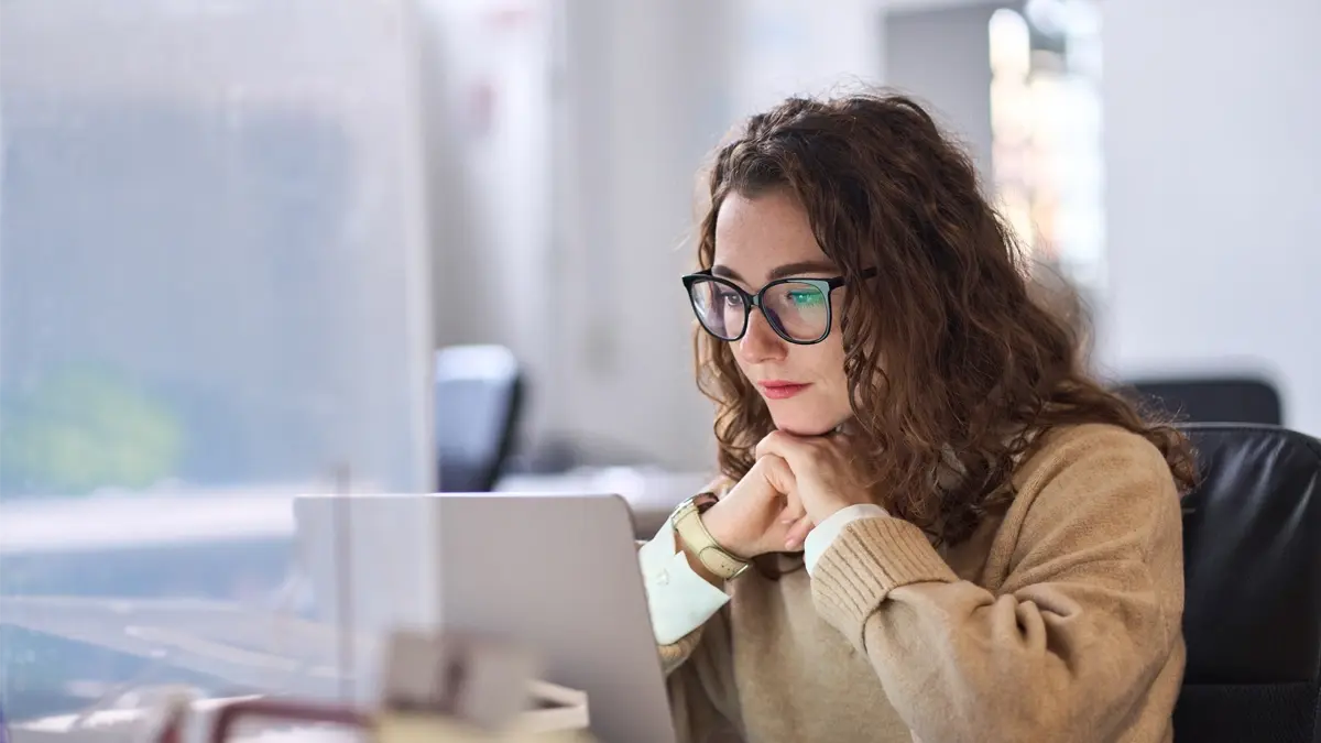 A lady with glasses sitting in an office looking at her computer.