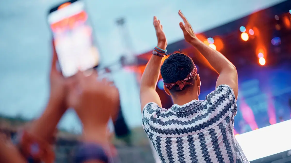 A man clapping with his hands up at a concert. Photo is taken from behind.