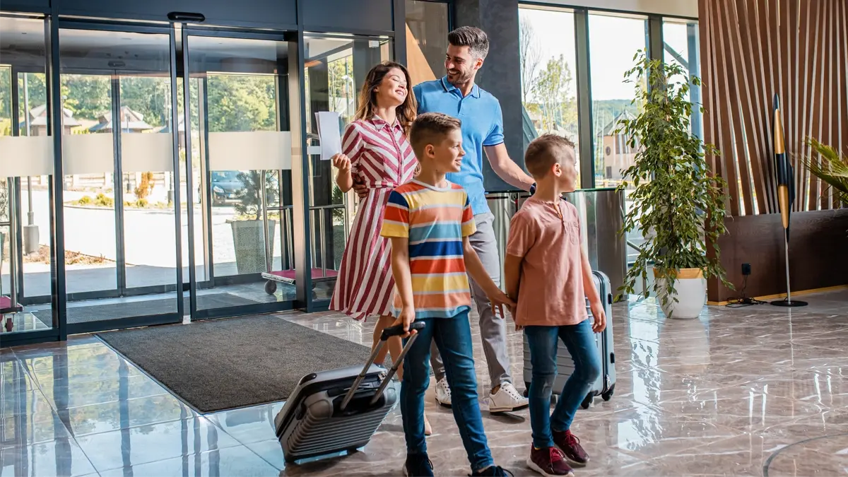 A family of 4 walking in a hotel lobby with their suitcases.